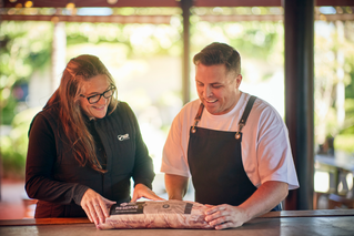 Silver Fern Farms staff member smiling while speaking to a person in chefs uniform, in the kitchen of a restaurant.